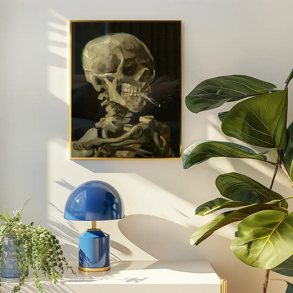 Painting of a skeleton smoking a cigarette, framed in gold, hanging on a light-colored wall next to a blue lamp and a large green plant.