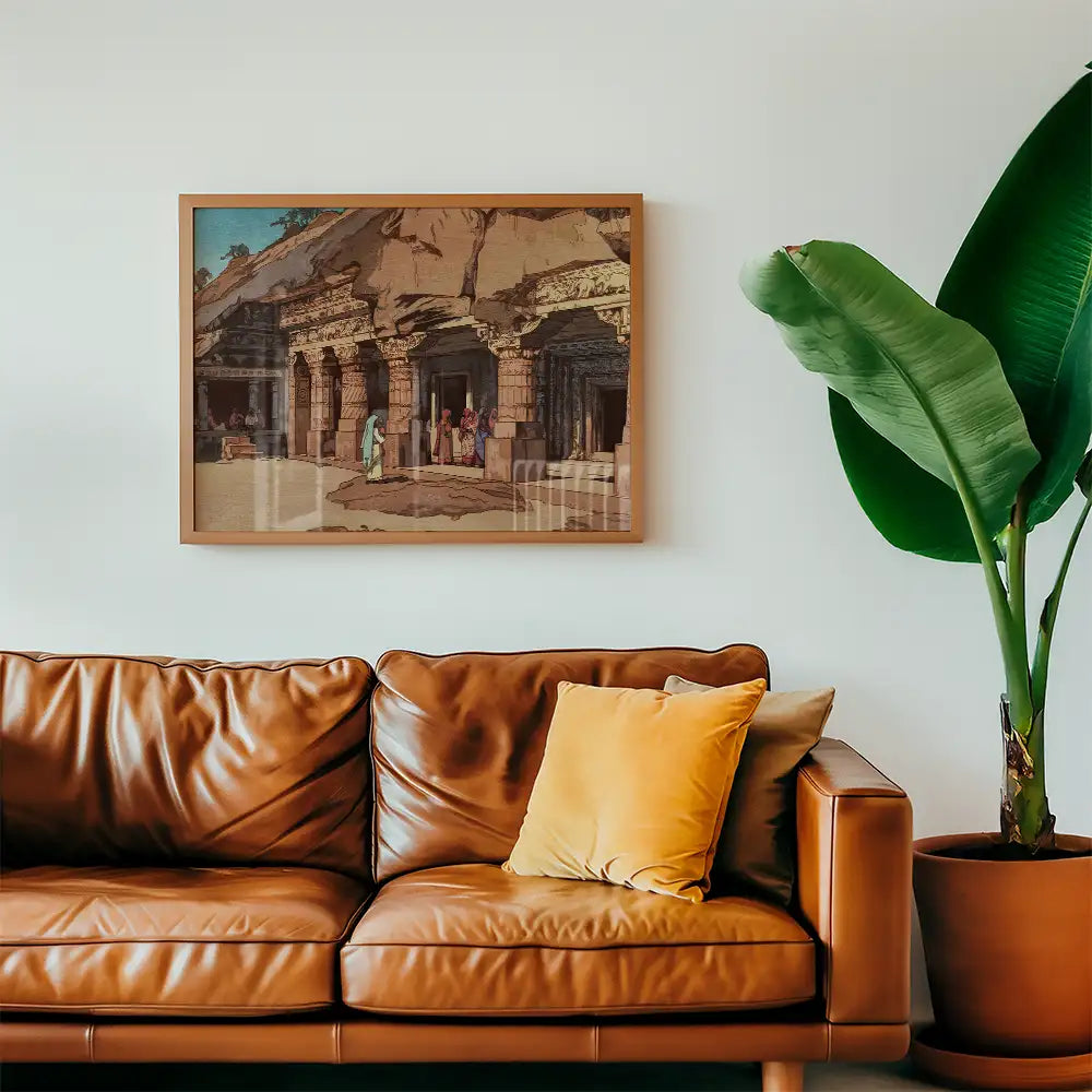 Framed painting of ancient cave architecture depicting figures at a historical site, displayed above a brown leather sofa with decorative cushions and a green plant.