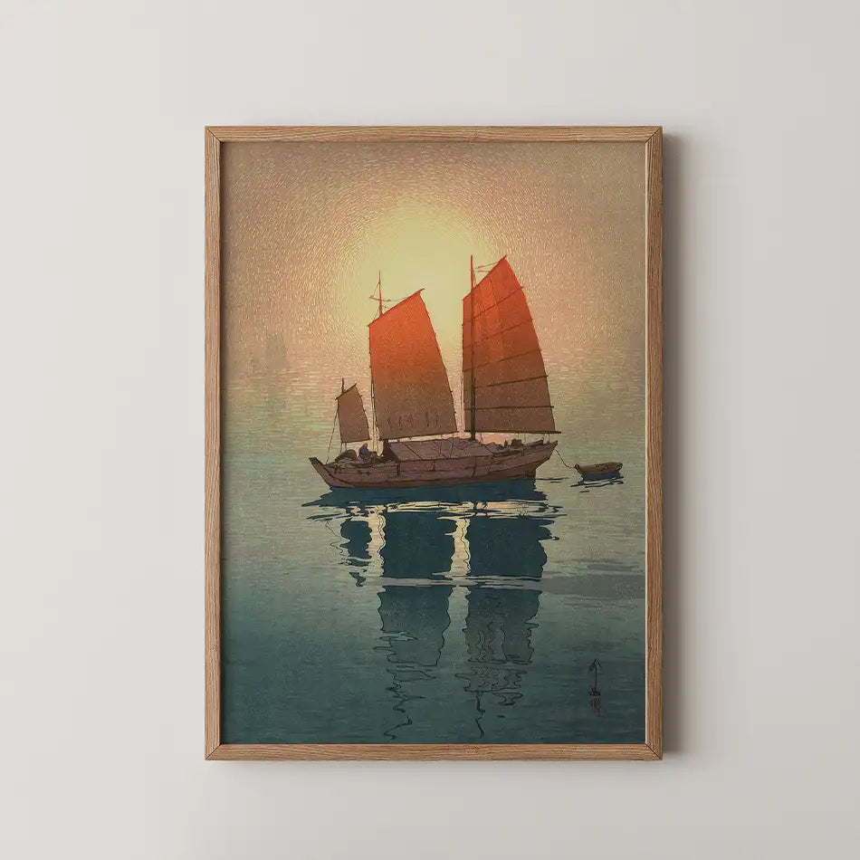 Framed painting of a sailing boat with red sails on calm waters, reflecting the glow of a setting sun in a serene atmosphere.