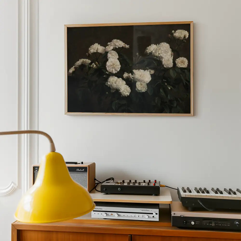 Framed painting of white flowers against a dark background, displayed on a wall with a yellow lamp and audio equipment in the foreground.