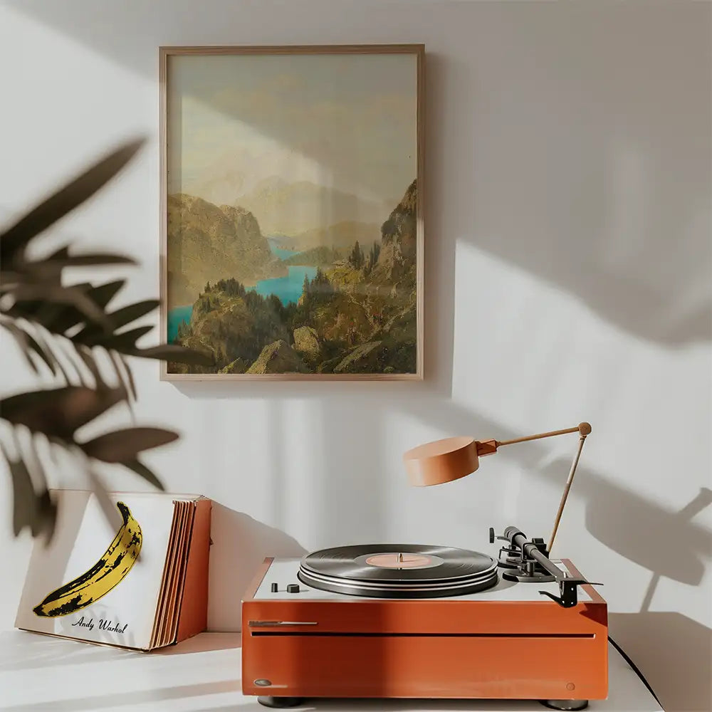 A vintage landscape painting featuring a serene mountain lake, framed and displayed on a wall above a mid-century record player and a stack of vinyl records.