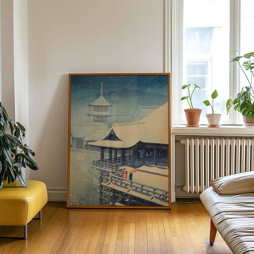 Framed painting of a snow-covered traditional building with two figures on a balcony, displayed in a modern living room setting with plants and furniture.