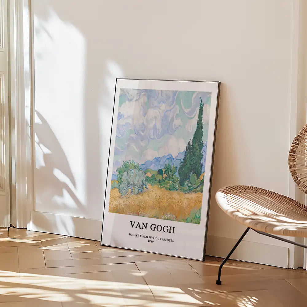 Framed poster of Vincent van Gogh's "Wheat Field with Cypresses" (1889) leaning against a wall, with a chair in the foreground and natural light casting shadows.
