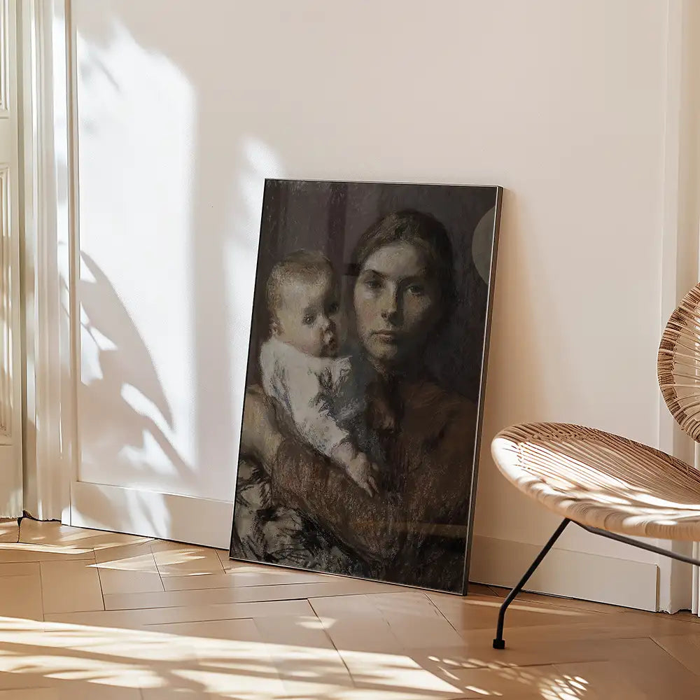 A framed painting of a mother holding a baby, leaning against a white wall in a well-lit room with warm wooden flooring and a rattan chair.
