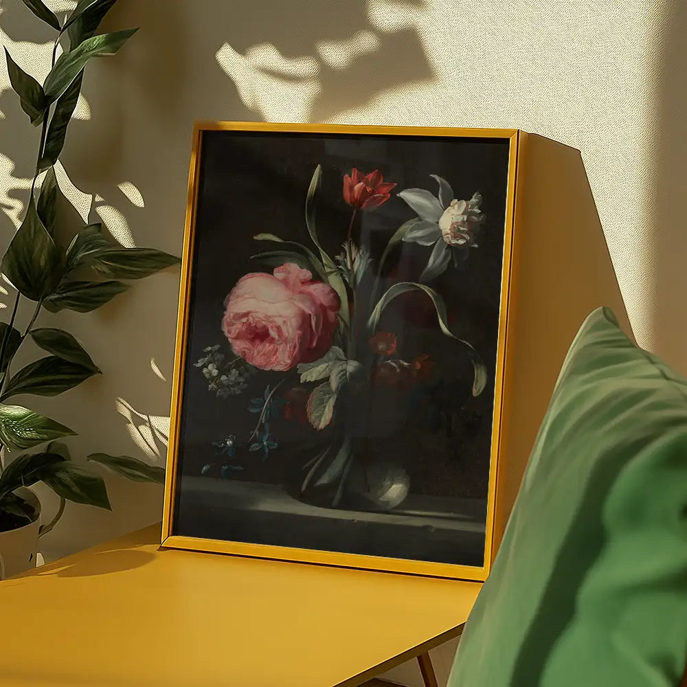 Floral painting in a yellow frame displayed on a table with green decor and plants in a bright room.