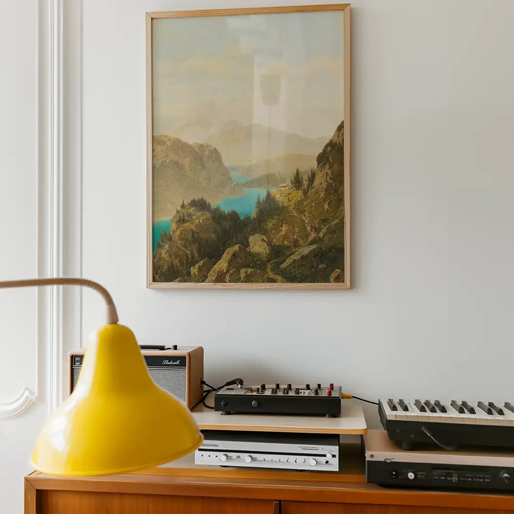 A scenic painting of mountains and a lake in a wooden frame, displayed on a wall above a modern audio setup and a bright yellow lamp.