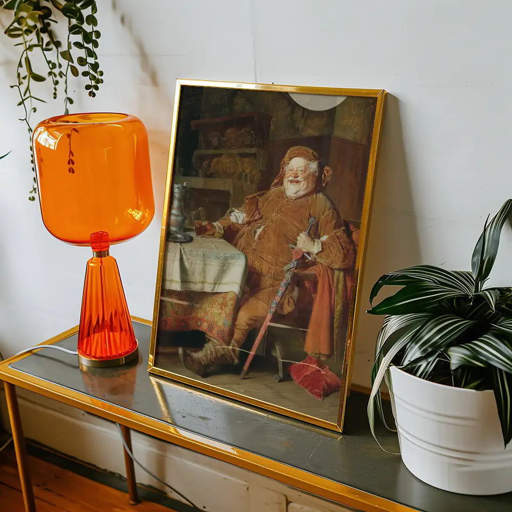 Framed painting of a jovial man in a brown outfit sitting at a table, next to an orange lamp and a potted plant.