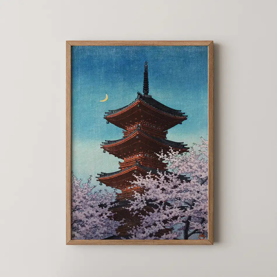 Framed painting of a traditional pagoda surrounded by cherry blossoms under a crescent moon and a blue sky.
