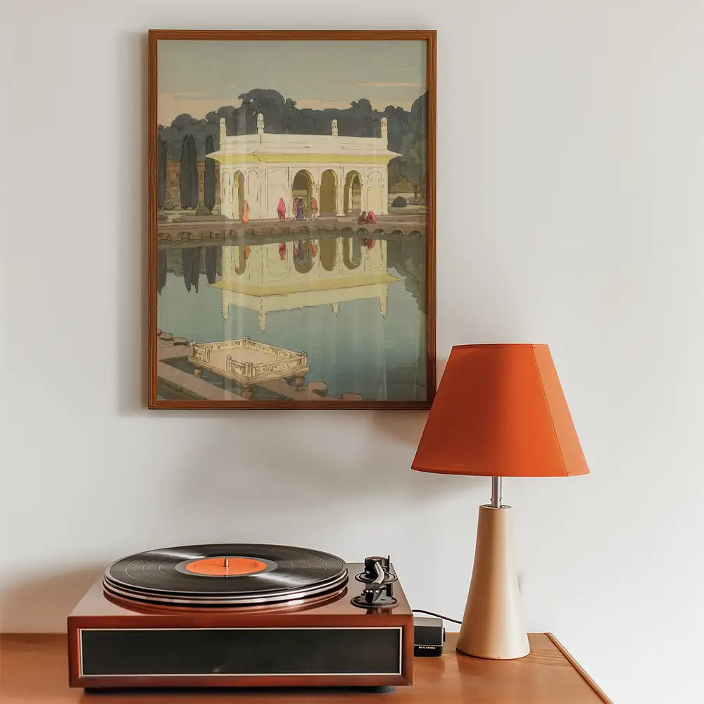 Framed painting of a historic building reflecting in water, displayed above a vintage record player and an orange lampshade.