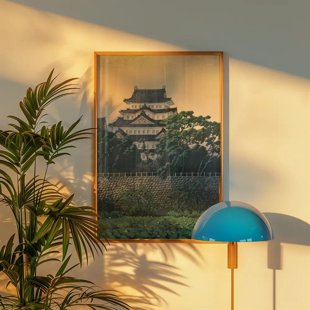 Framed painting of a traditional Asian castle surrounded by greenery, displayed on a wall next to a modern lamp and indoor plant.