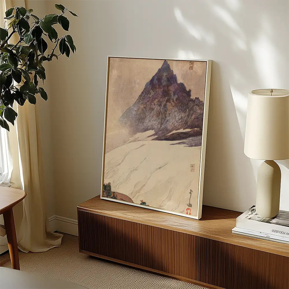 Framed painting of a mountain landscape displayed on a wooden console, with a lamp and decorative items in a bright interior setting.