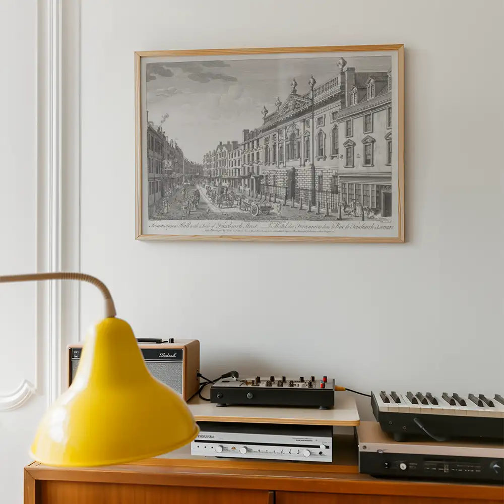 Black and white framed vintage cityscape illustration on a wall above a wooden console with a yellow lamp, retro speakers, and musical equipment.