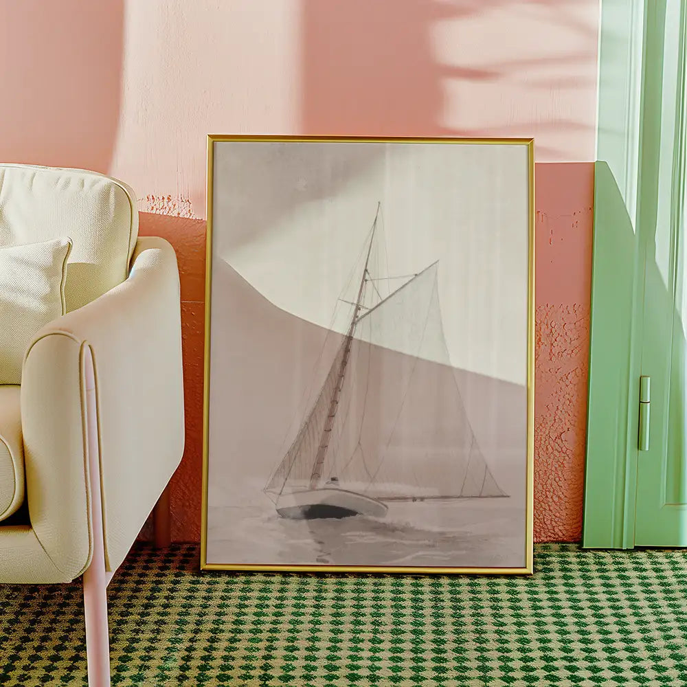 Black and white painting of a sailboat, framed in gold, leaning against a pastel pink wall next to a light-colored armchair on a green checkered rug.