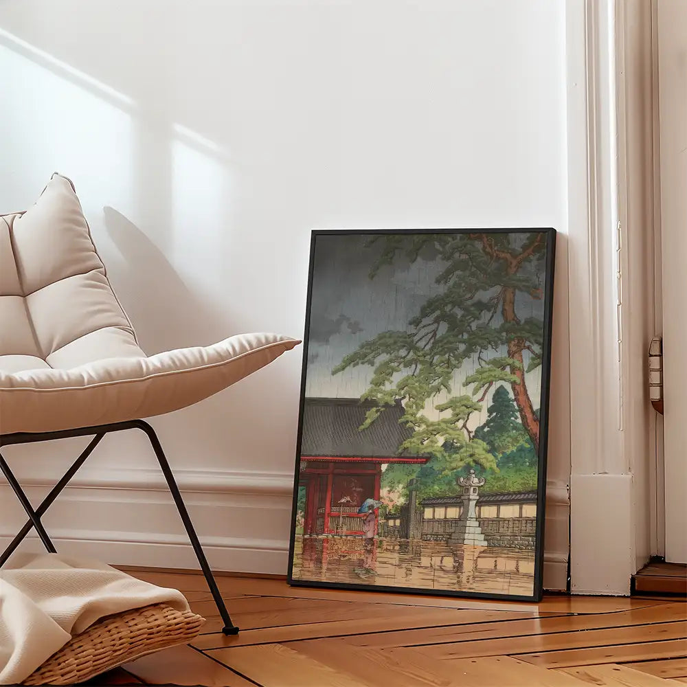 Framed painting of a serene landscape featuring a traditional building and greenery, leaning against a wall next to a modern chair.