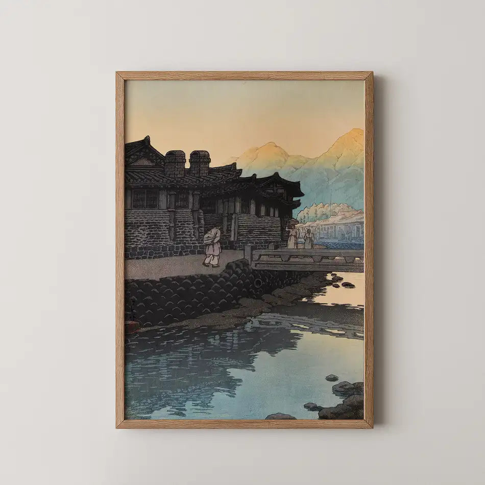 Framed painting of a traditional building by a river at sunset, featuring soft colors and serene reflections.