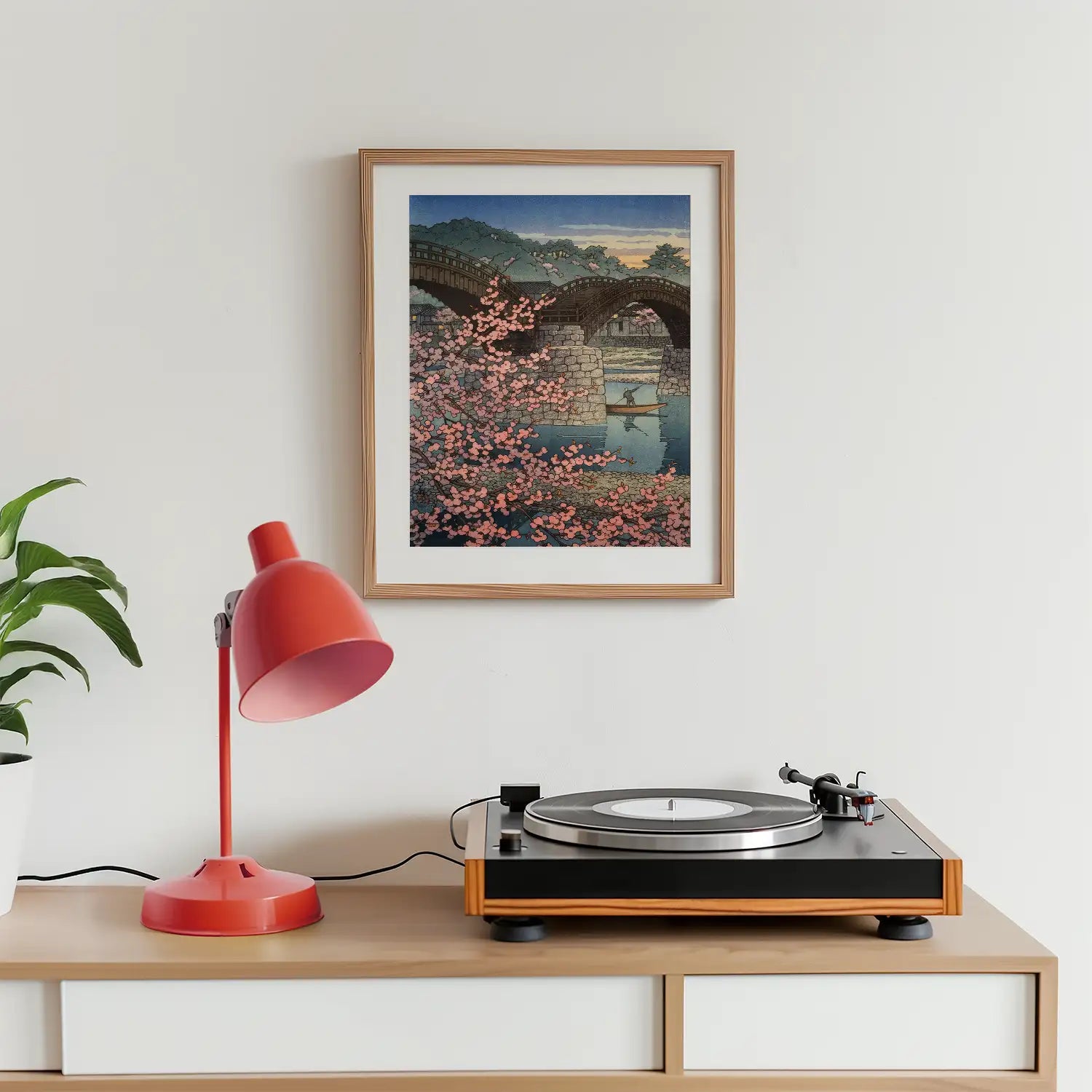 Framed painting of a bridge surrounded by cherry blossoms, displayed above a record player and a desk lamp.