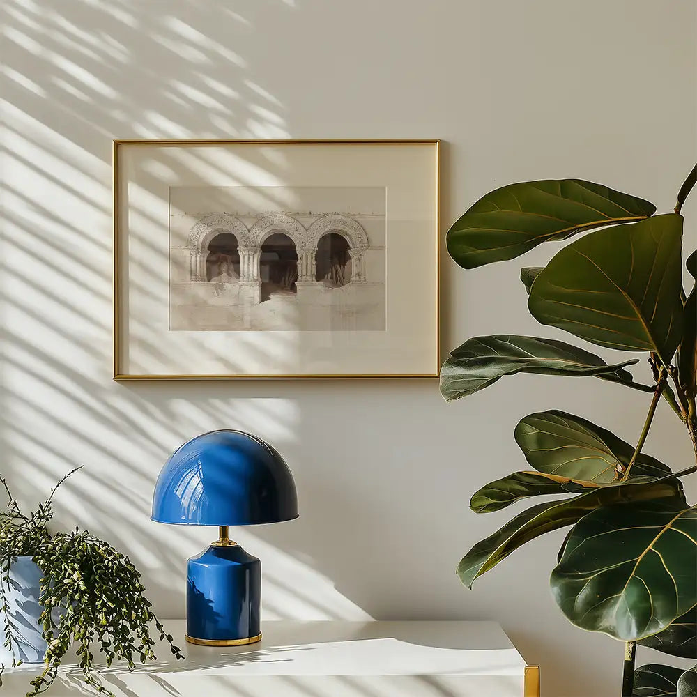 Framed abstract painting of arches on a wall with a blue table lamp and indoor plants in a bright room.