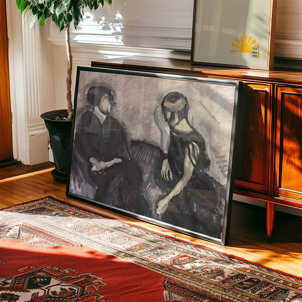 A framed black and white painting of two women sitting together, placed on a wooden floor next to a potted plant and an ornate rug.
