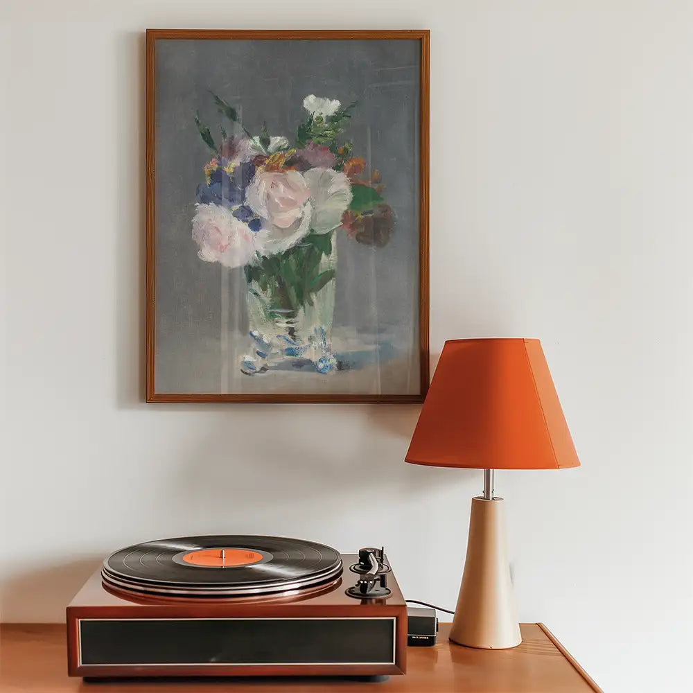 Painting of a floral arrangement in a glass vase, displayed in a wooden frame on a wall above a vintage record player and an orange lampshade.