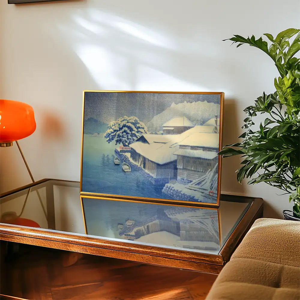 Painting of a serene snowy landscape with wooden houses and boats, displayed on a coffee table next to a potted plant and a modern lamp.