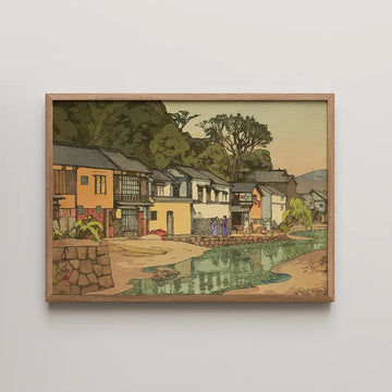 A framed painting depicting a serene riverside village scene with traditional houses and lush greenery.