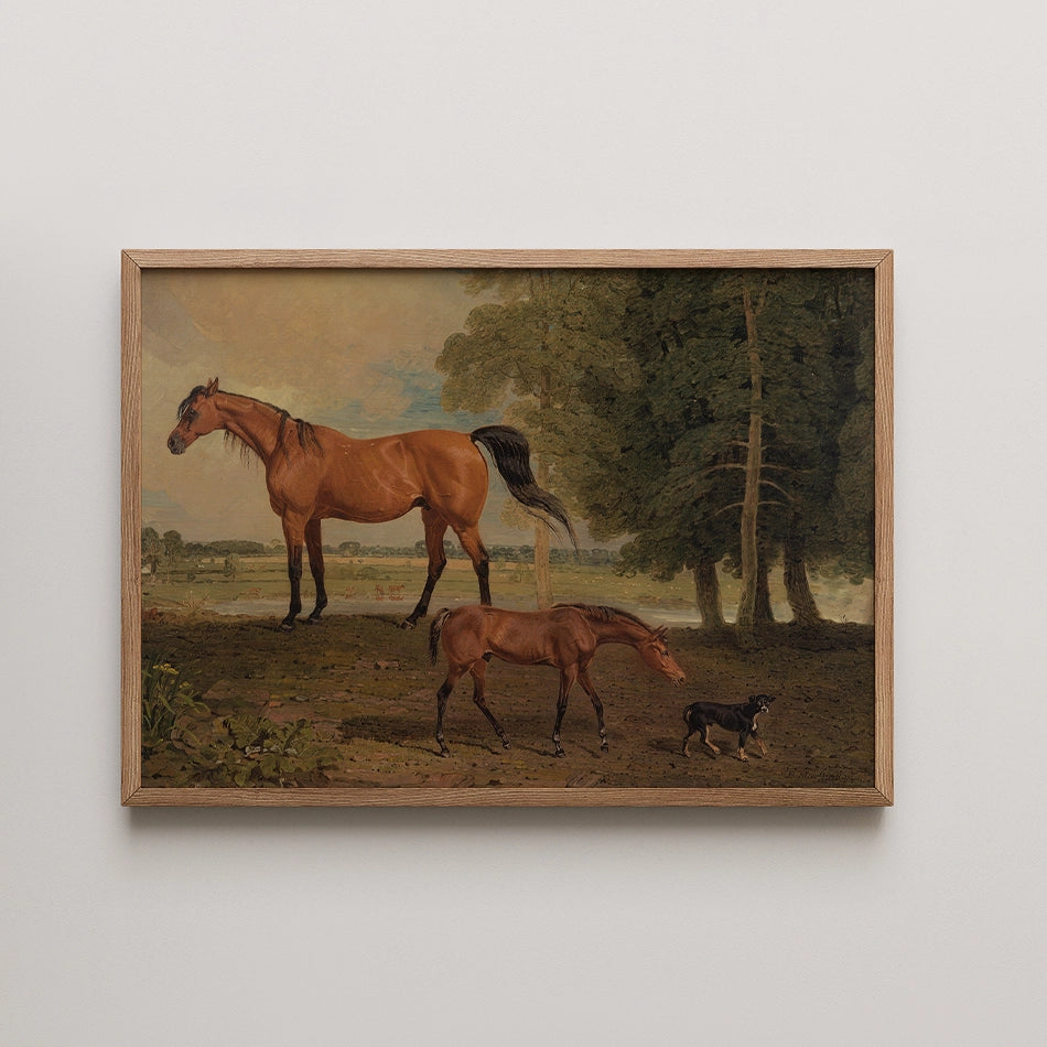 Framed painting of a brown horse, a foal, and a small dog in a natural landscape with trees and a water body in the background.
