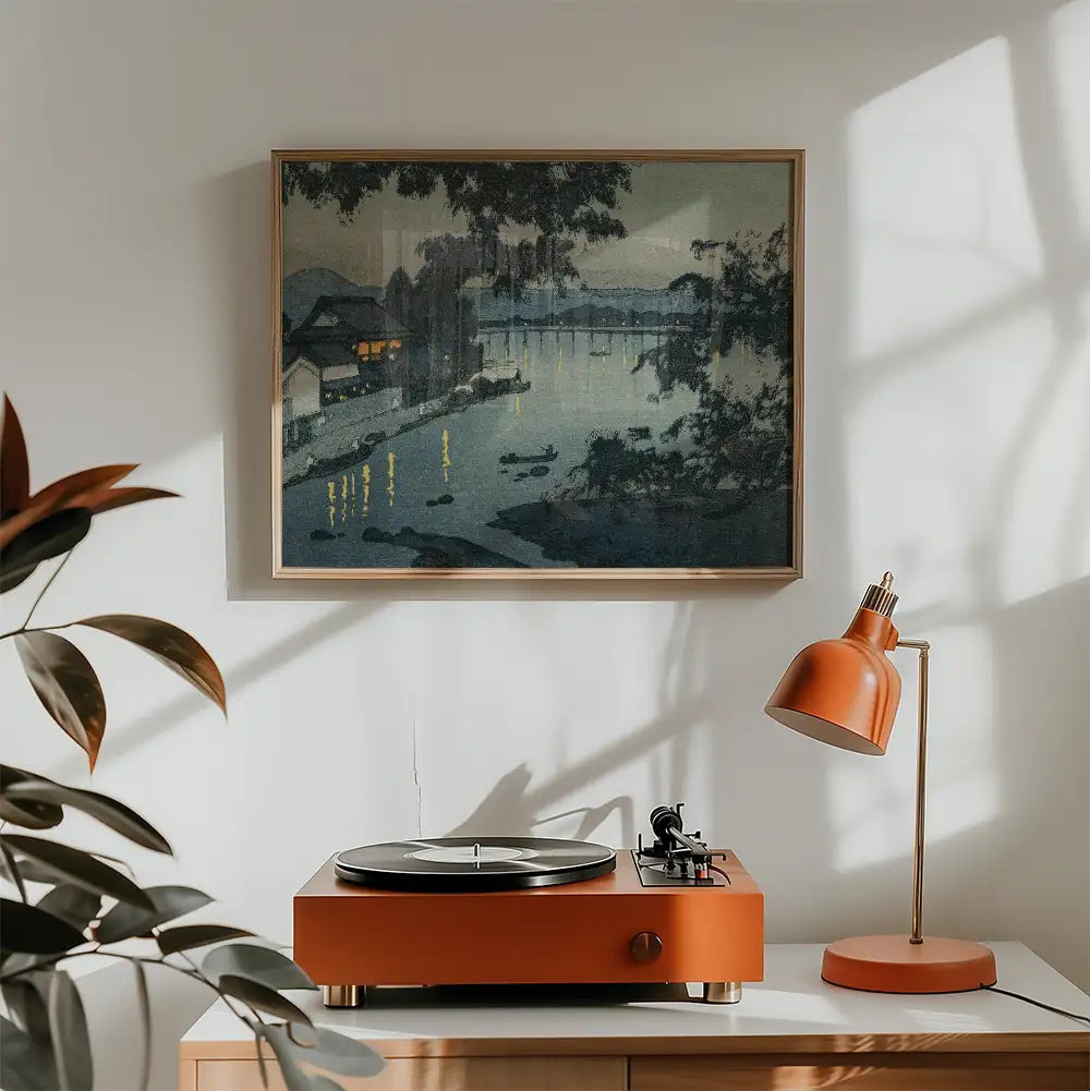 Framed painting of a serene river scene with boats and illuminated reflections on the water, hung above an orange record player and lamp in a modern interior setting.