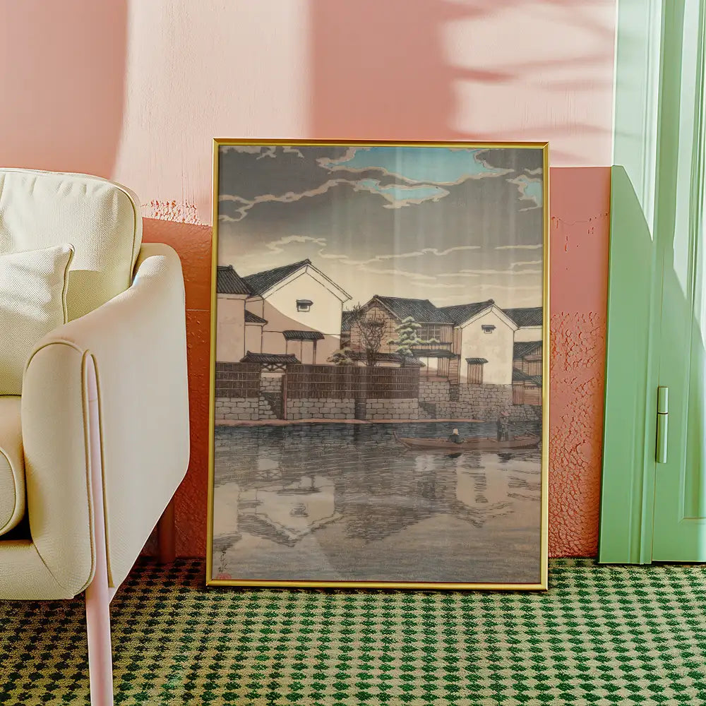 Framed painting of traditional houses by a waterfront with muted colors, displayed in a modern interior setting.