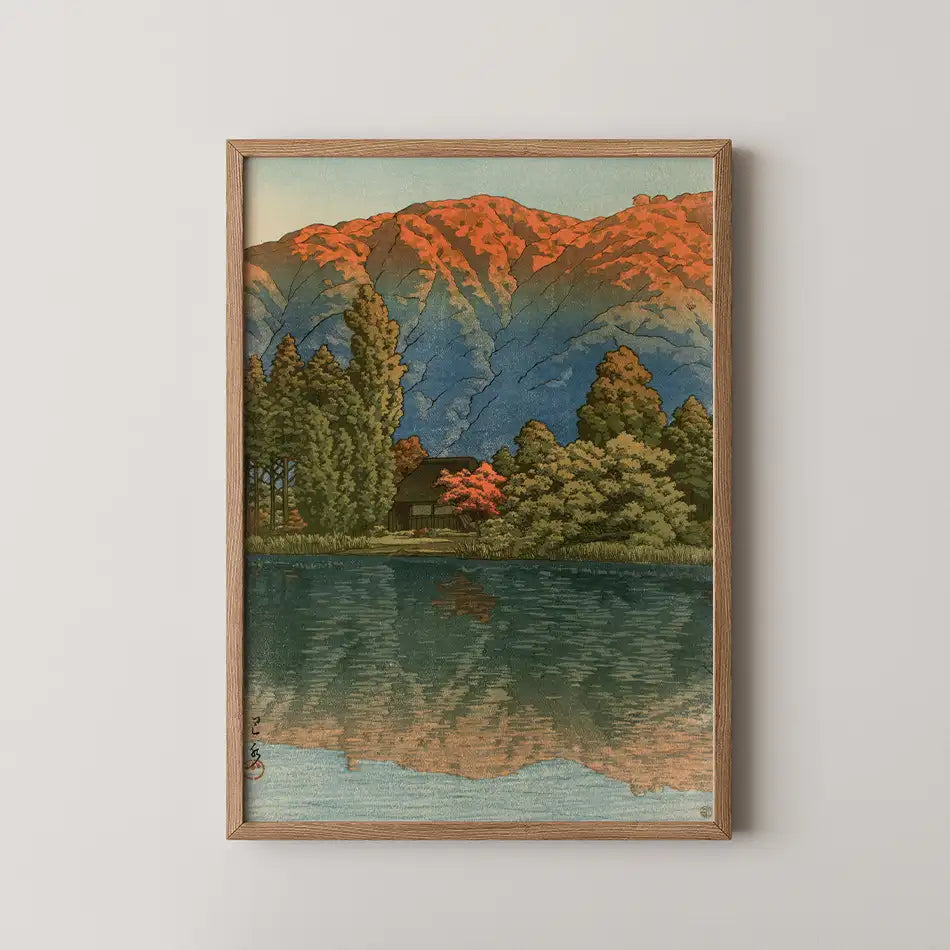 Framed painting of a serene landscape featuring a reflection of mountains, trees, and a house in a calm lake with vibrant autumn colors.