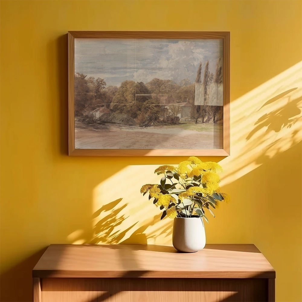 A framed landscape painting on a yellow wall above a wooden dresser with a vase of yellow flowers.
