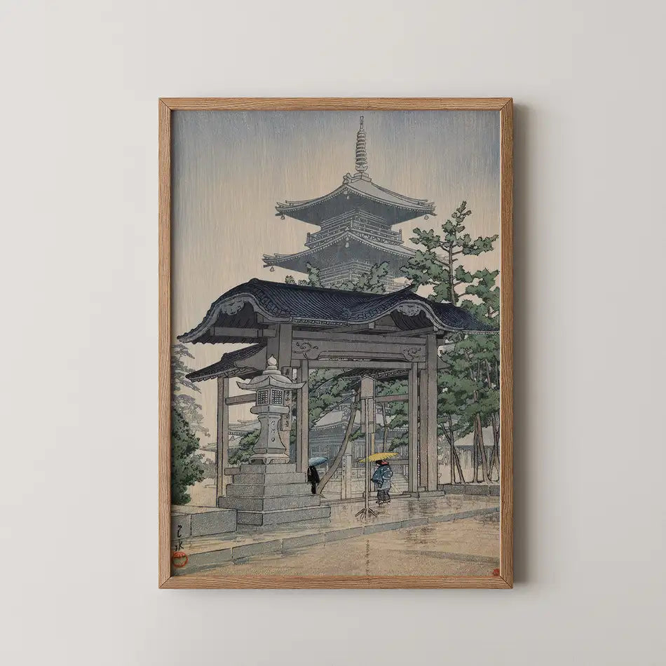 Framed painting of a traditional Asian temple scene with a stone gate and figures walking under umbrellas in a rainy setting.