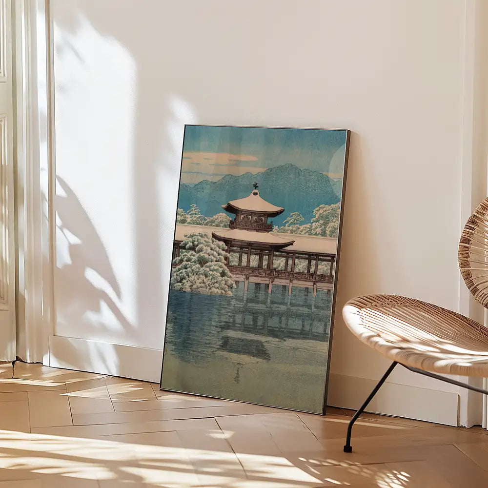 Painting of a traditional Japanese building surrounded by trees and mountains, leaning against a wall with a modern chair nearby.