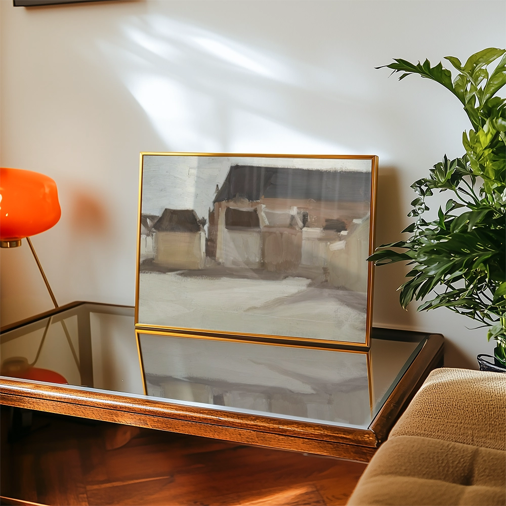 Abstract painting displayed in a golden frame on a glass-top table, with a vibrant orange lamp and potted plant in the background.