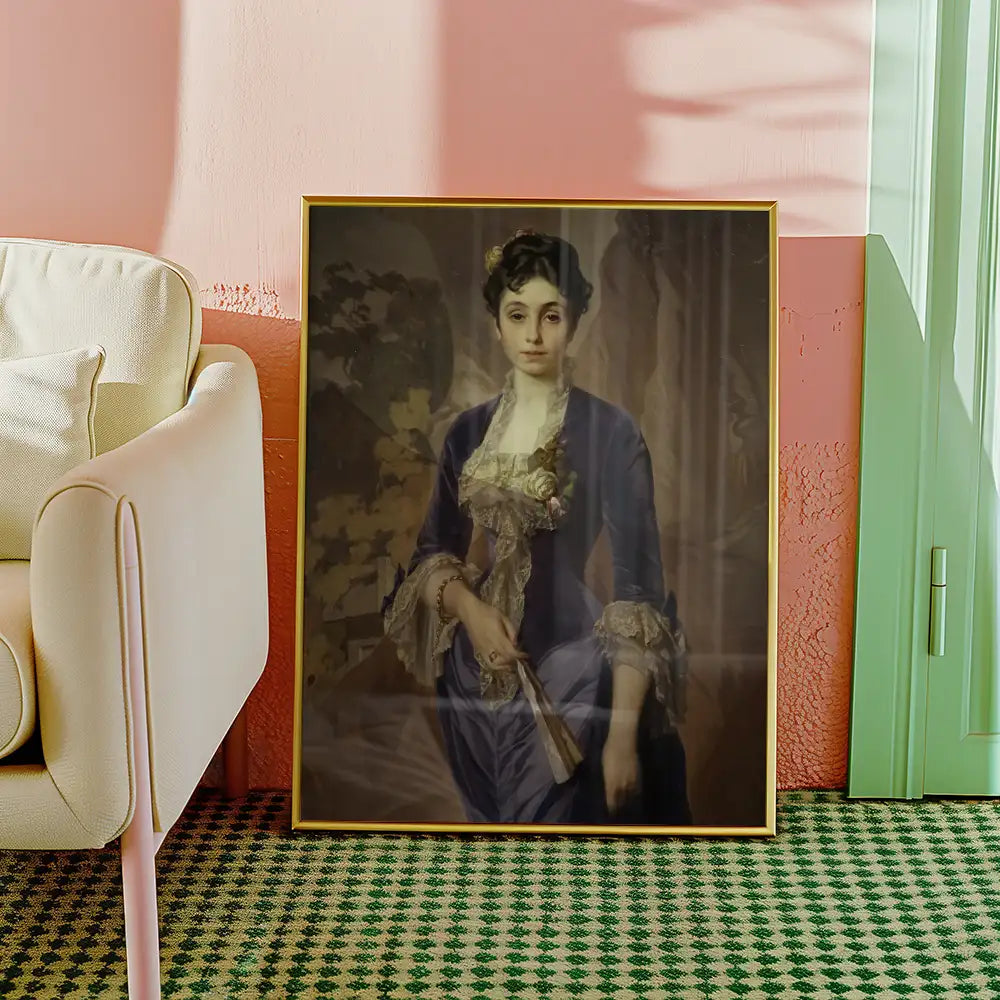 Portrait of a woman in a blue dress with lace details, framed and displayed against a pink wall, next to a modern cream-colored chair.