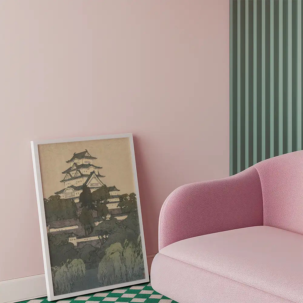 Framed painting of a Japanese castle set against a muted background, leaning against a pastel pink wall next to a pink sofa.