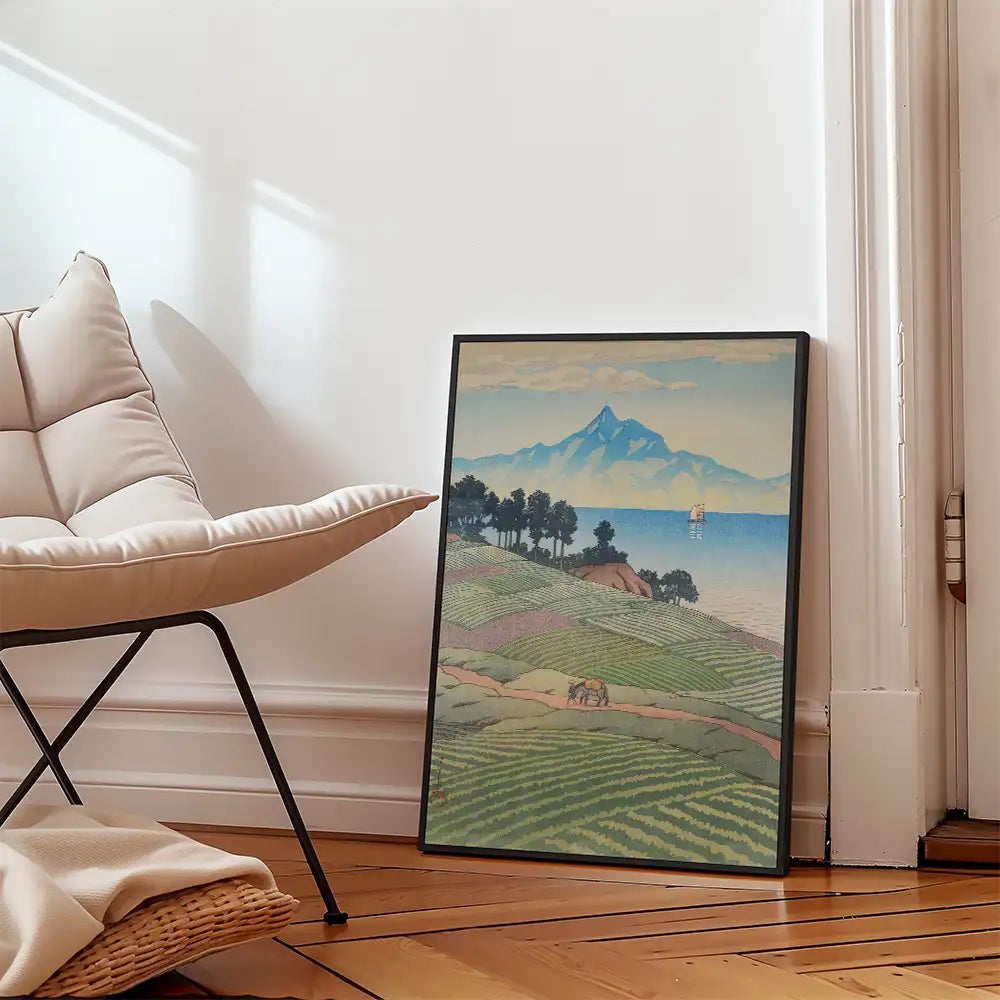 Framed painting of a tranquil landscape with mountains, trees, and a body of water, leaning against a wall next to a modern chair.