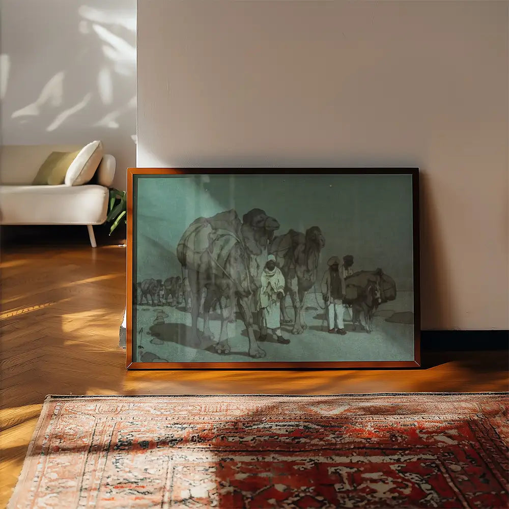 Framed painting of camels and figures in a desert landscape, displayed indoors on a wooden floor next to a patterned rug.