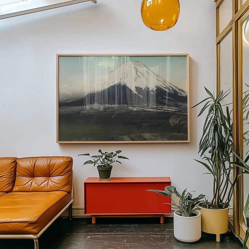 Framed painting of a mountain landscape displayed in a modern living room with orange couch and decorative plants.