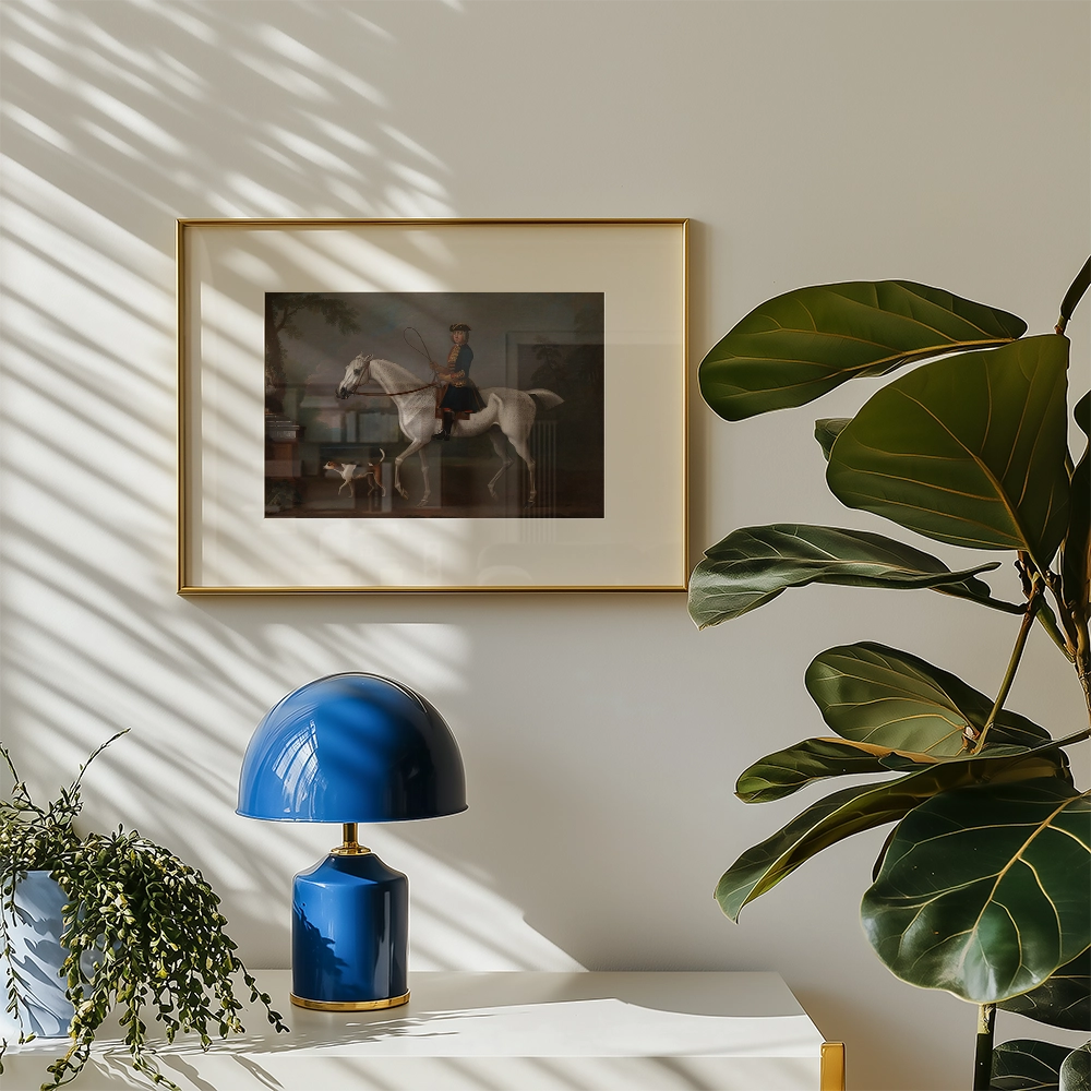 Framed painting of a rider on a white horse displayed on a wall, with a blue lamp and green foliage in the foreground.