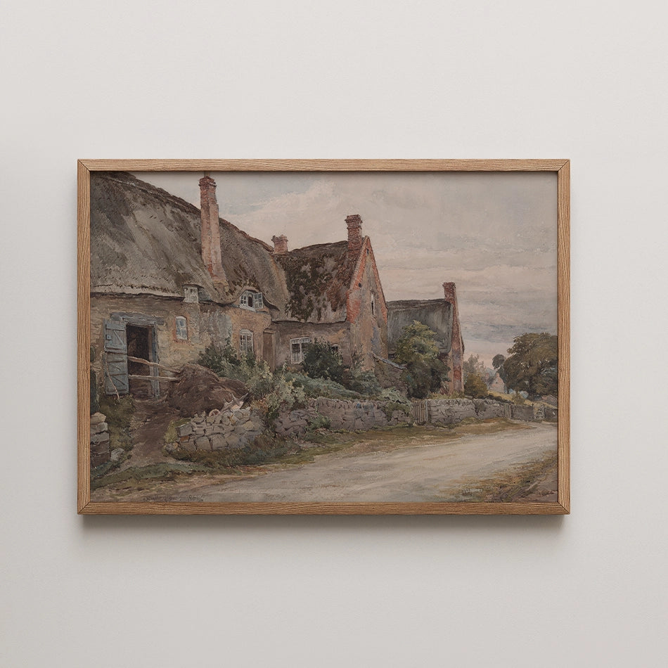 Framed painting of rustic cottages along a dirt road, featuring thatched roofs and lush greenery.