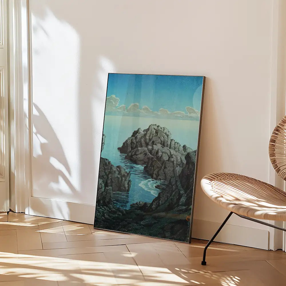 Framed painting of rocky coastline and water, leaning against a wall in a modern interior setting.