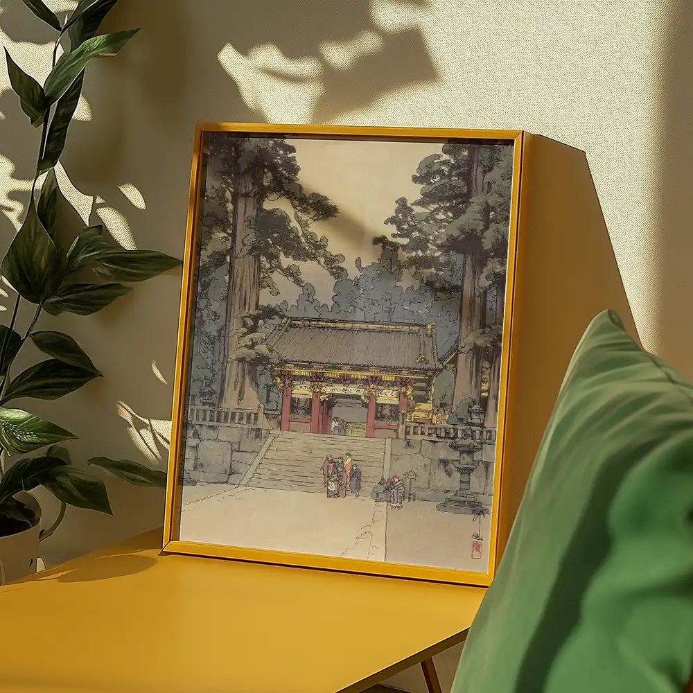 Framed painting of a traditional temple surrounded by trees, displayed on a yellow table with decorative green pillows and shadows in the background.