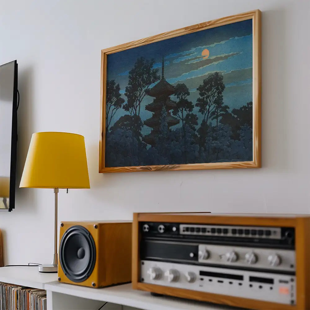 A framed painting of a pagoda surrounded by trees under a night sky, with a yellow lamp and a vintage audio system in a modern living room setting.