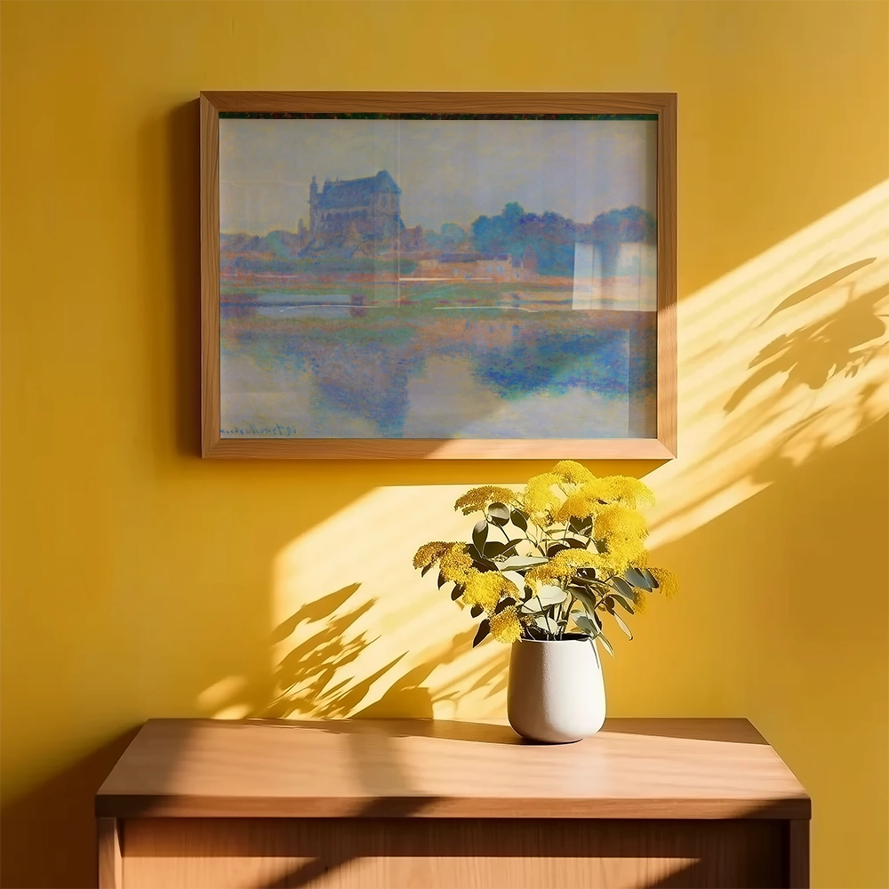Framed painting of a serene landscape featuring a building by a body of water, displayed against a bright yellow wall, with a vase of yellow flowers in the foreground.