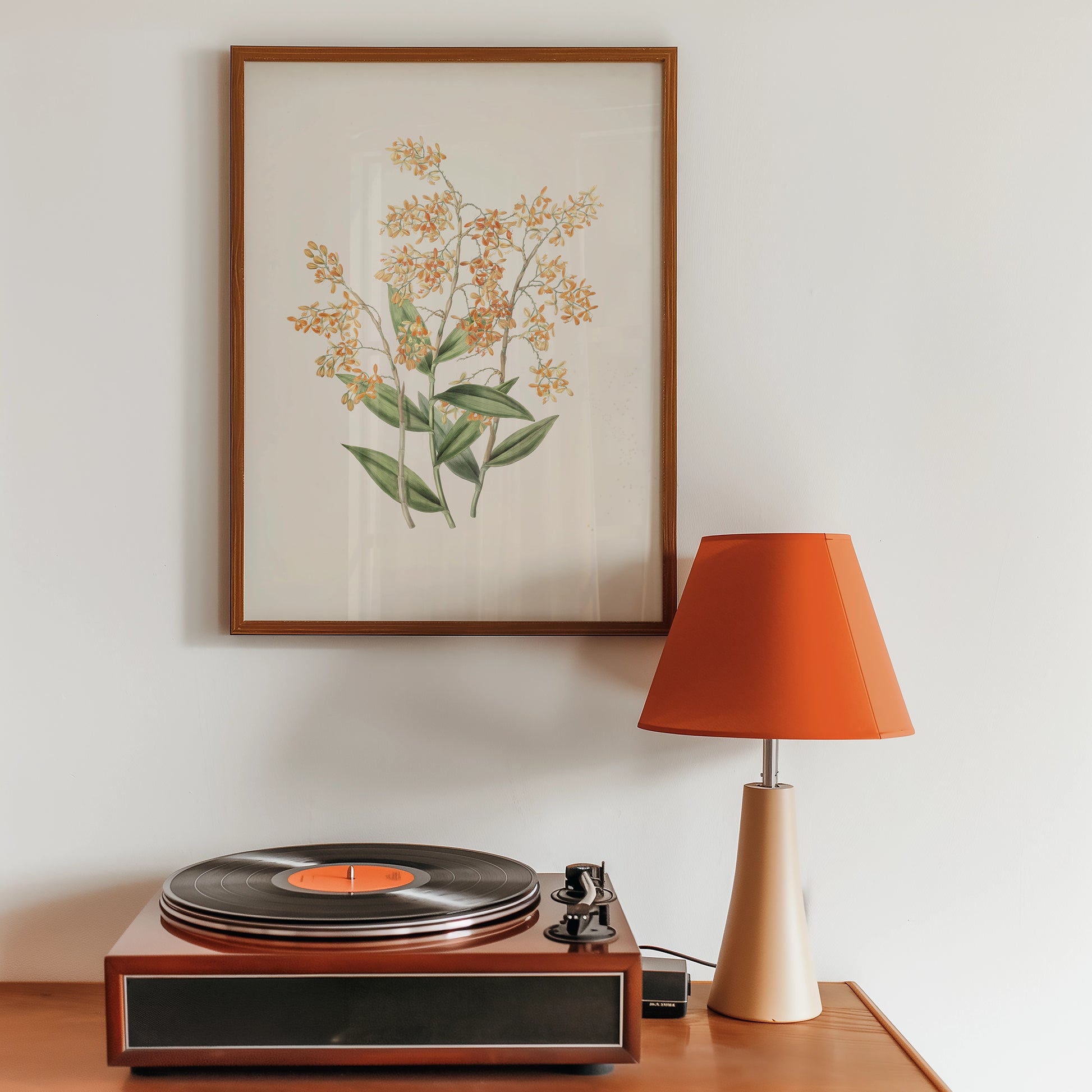 Framed painting of orange flowers on a beige background, displayed above a vintage record player and an orange lamp on a wooden table.