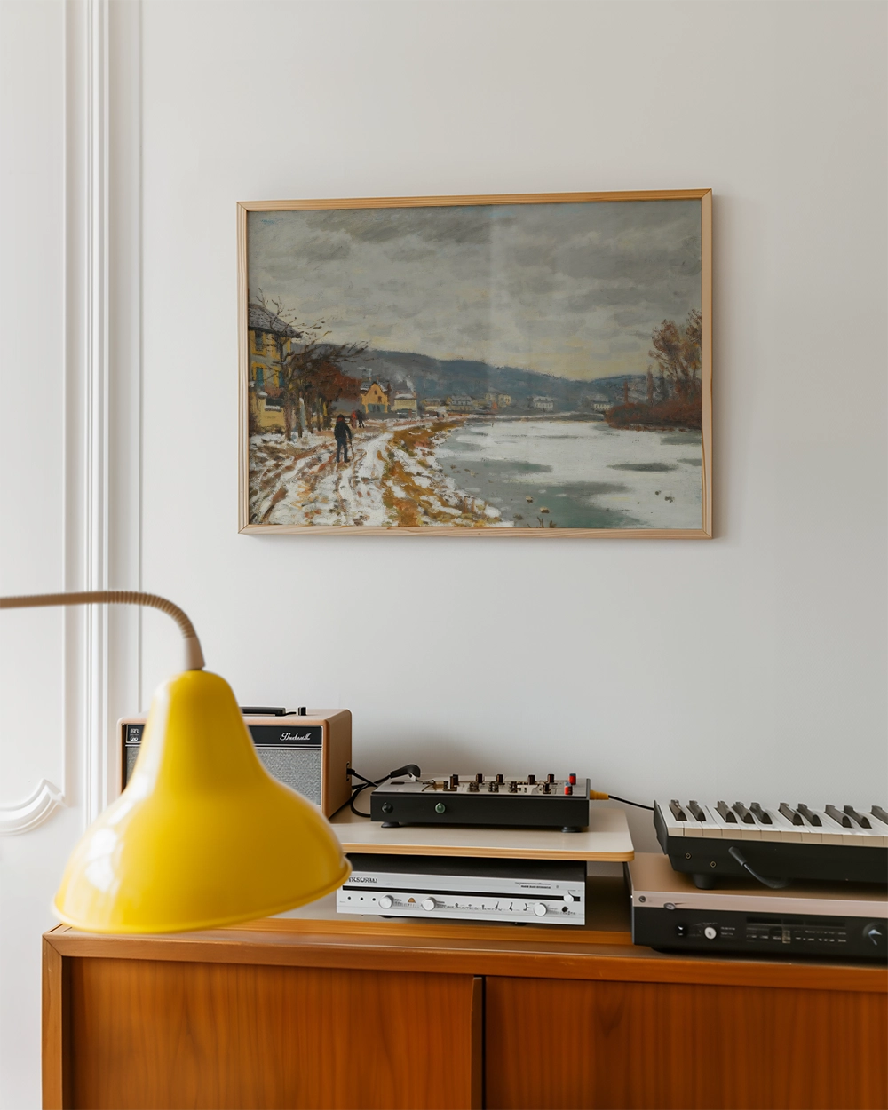 Framed painting of a winter landscape with a river, featuring a person walking along a snowy path and a collection of vintage audio equipment nearby.