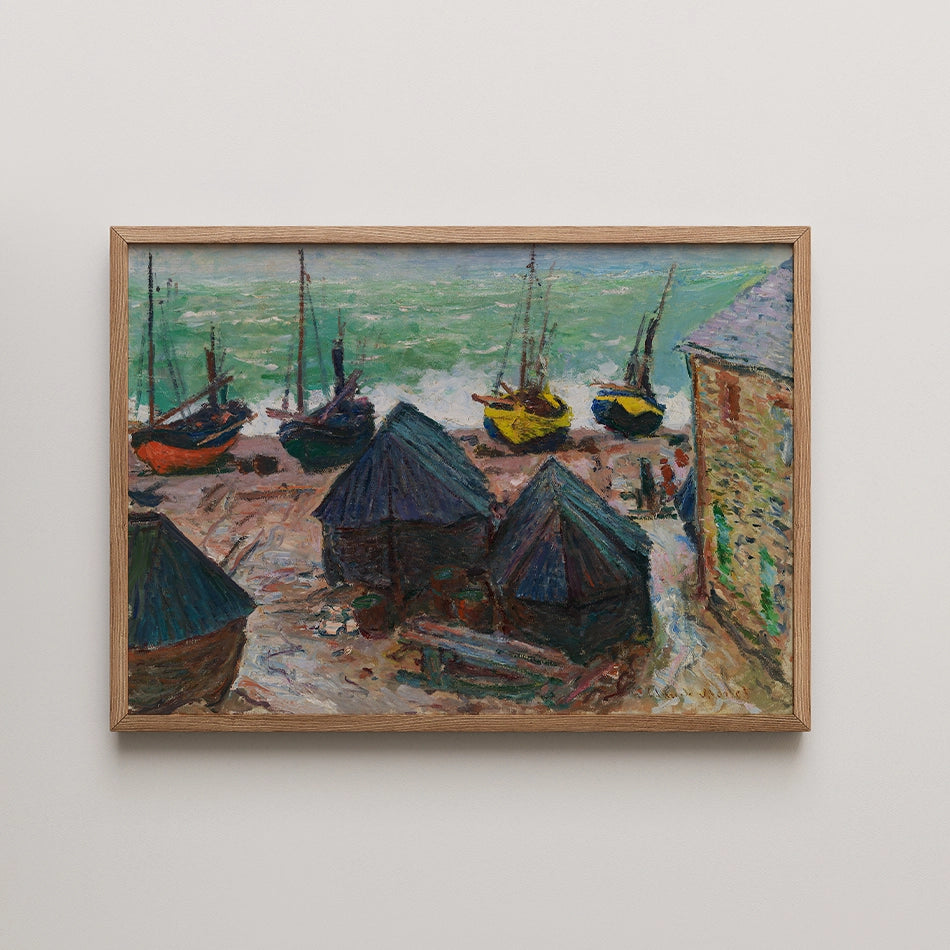 Painting of a coastal scene featuring colorful boats anchored near a shoreline, with small fishing huts and a building in the foreground, framed in natural wood.