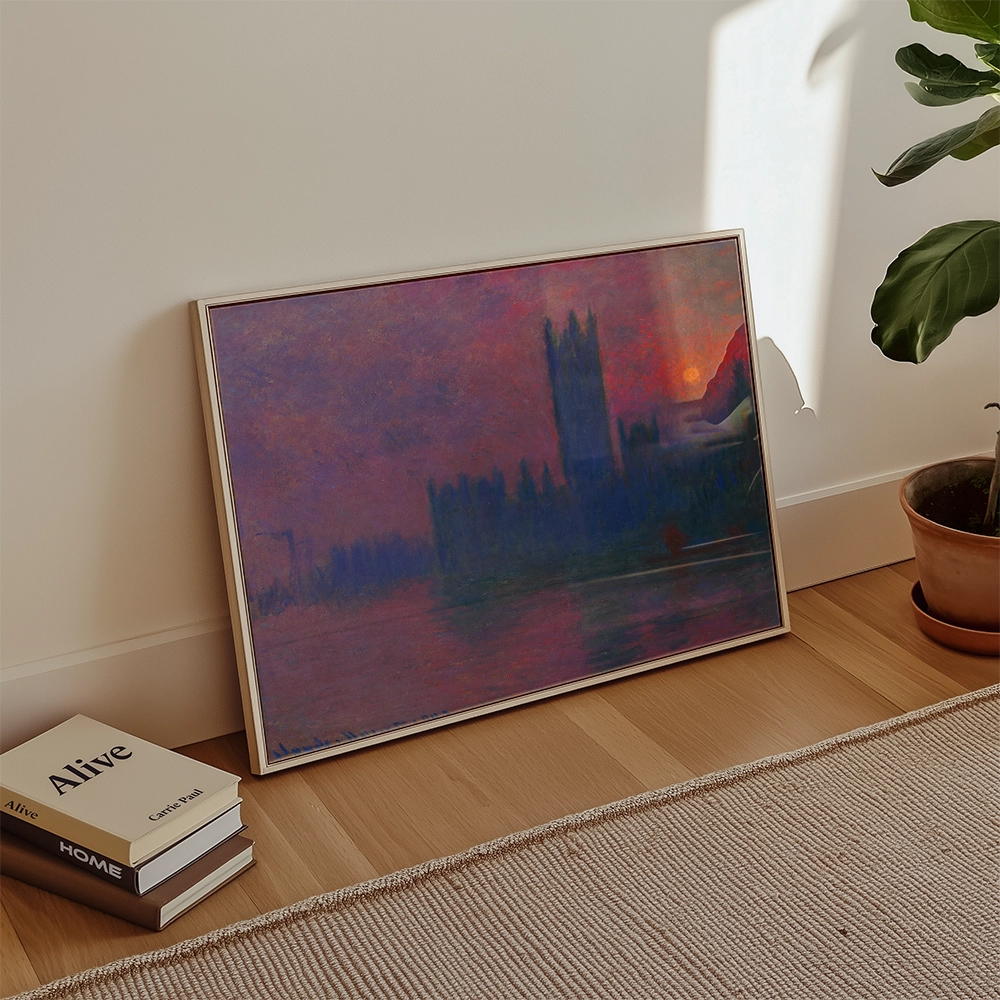 Framed painting leaning against a wall featuring a vibrant sunset over a silhouette of tall buildings, with a potted plant and stacked books in a cozy interior setting.