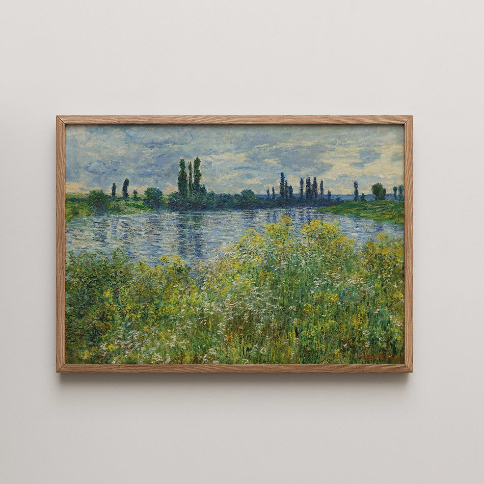 Landscape painting depicting a serene riverside scene with greenery and a cloudy sky, framed in wood.