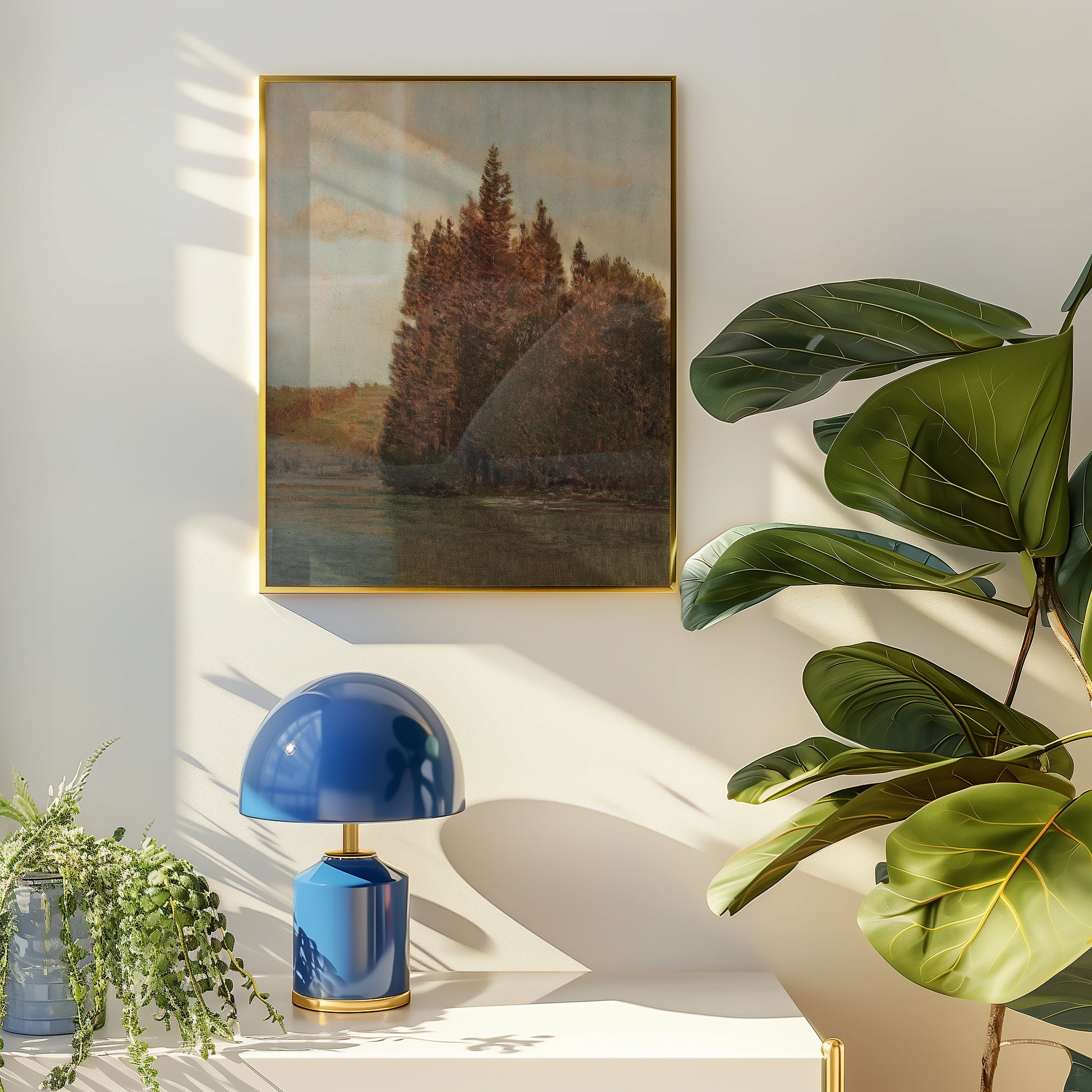 Painting of a serene landscape featuring trees beside a calm body of water, framed in gold, displayed on a softly lit wall with a stylish blue lamp and lush green plants nearby.